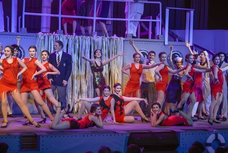 Estudiantes del Walkerville Collegiate Institute realizan una vibrante presentación de danza con vestidos rojos en un escenario colorido.
