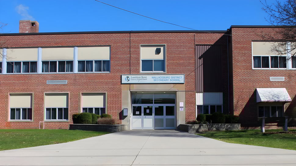 El edificio de ladrillo de dos pisos de la Wallaceburg District High School con grandes ventanas se encuentra bajo un cielo azul claro.