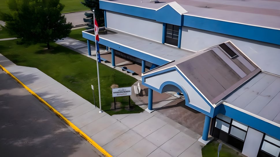 El moderno edificio de varios pisos de la Warburg School con fachada azul y gris está rodeado de un área de césped y un camino pavimentado.