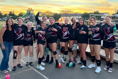 Un grupo de jóvenes deportistas de la Warburg School posan juntos en el campo de deportes frente a los equipos de juego.