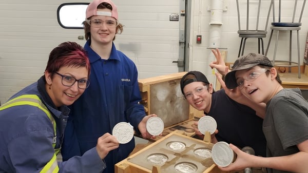 Estudiantes de la Warburg School trabajan en el taller y examinan piezas de cerámica en una mesa de madera.
