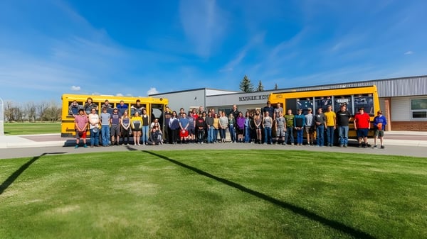 Un grupo de estudiantes y adultos está frente a un autobús escolar amarillo en el terreno de la Warner School.