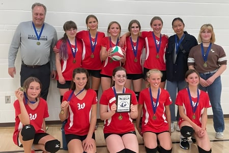 El equipo de voleibol de la Warner School posando en el gimnasio con un trofeo junto a las entrenadoras.