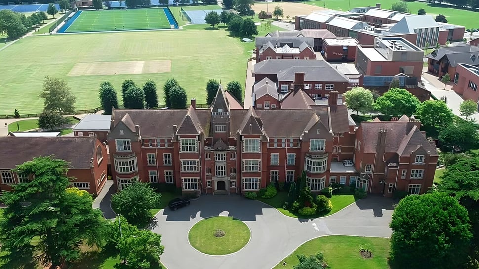 El histórico edificio de ladrillo de la Warwick School se encuentra rodeado de un prado verde y árboles en primer plano.