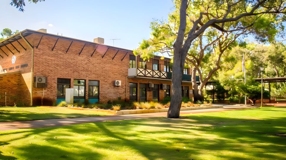 El edificio de ladrillo con balcón y un césped verde frente a Warwick Senior High School está rodeado de árboles y cielo azul.