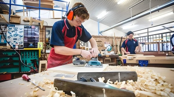 Una estudiante o un estudiante de Warwick Senior High School trabaja con una herramienta eléctrica en un proyecto de madera en el taller.