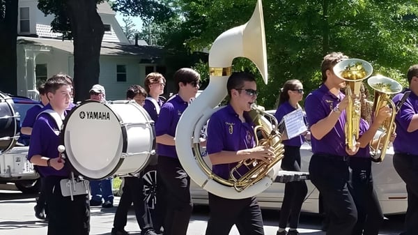 Un grupo de músicos en uniformes morados toca en la calle frente a edificios en el campus de la Warwick Valley High School.