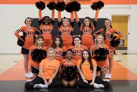 Un grupo de animadoras de la Wasatch Academy posando en uniformes naranjas y negros en el gimnasio.