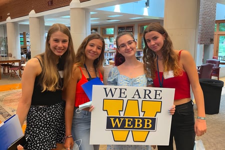 Cuatro alumnas de la Webb School sostienen juntas un cartel con la inscripción 'SOMOS WEBB' en un café.