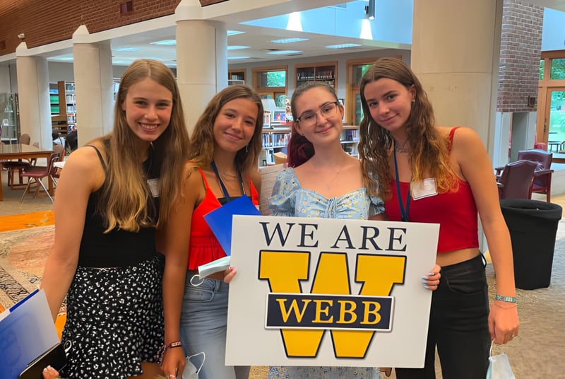 Cuatro alumnas de la Webb School sostienen juntas un cartel con la inscripción 'SOMOS WEBB' en un café.