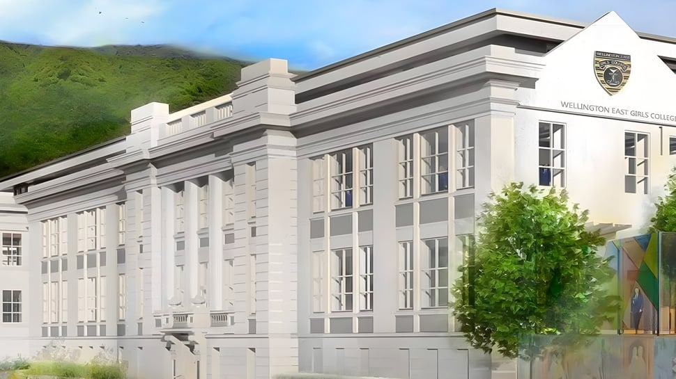 El gran edificio blanco del Wellington East Girls’ College está rodeado de naturaleza verde y montañas al fondo.