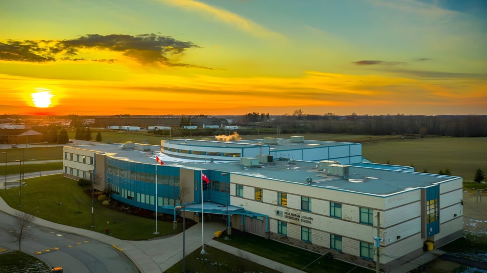 El moderno edificio de la Wellington Heights Secondary School con fachada azul se encuentra frente a un colorido atardecer.