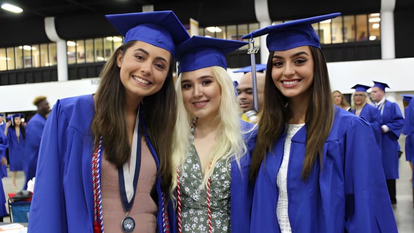 Tres estudiantes de la Wellington Heights Secondary School celebran su graduación en batas y birretes azules.