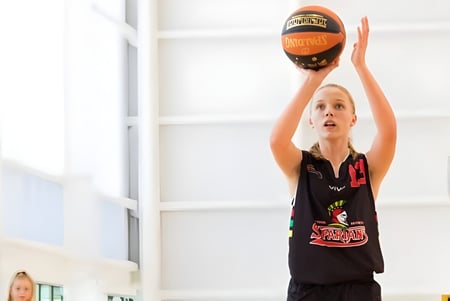 Una joven jugadora de baloncesto de la Wellington Point State High School salta en el gimnasio y alcanza el balón.