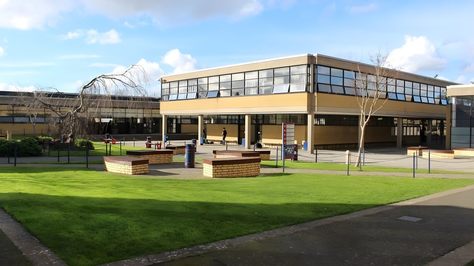 Un moderno edificio de varios pisos con grandes ventanas en el campus del Wesley College está rodeado de césped verde y bancos.