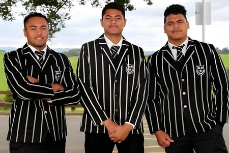 Tres estudiantes del Wesley College están juntos en un área exterior cubierta de hierba con árboles de fondo.