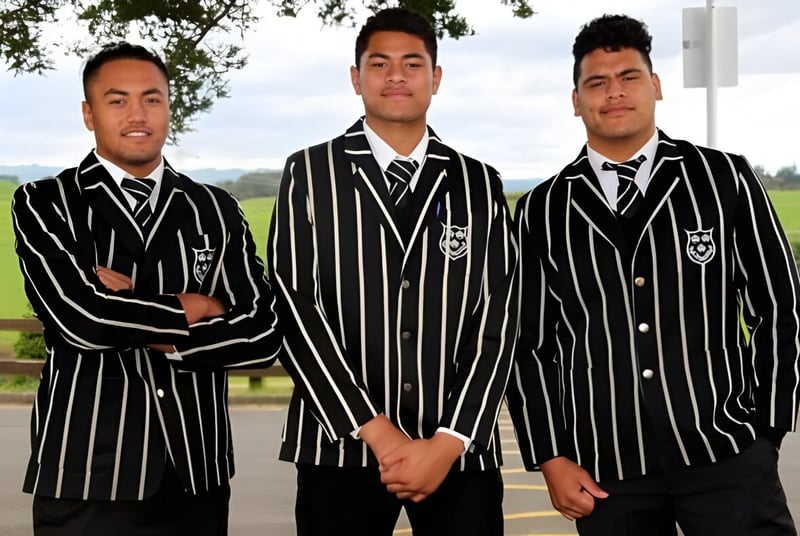 Tres estudiantes del Wesley College están juntos en un área exterior cubierta de hierba con árboles de fondo.