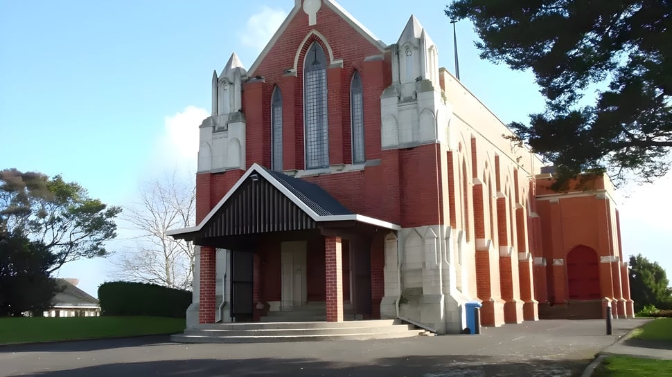 La iglesia de ladrillo rojo con arquitectura gótica se encuentra en el campus del Wesley College y está rodeada de árboles.