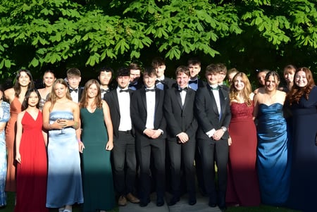 Un grupo de personas vestidas de forma formal está frente a un follaje verde en el campus de la West Buckland School.