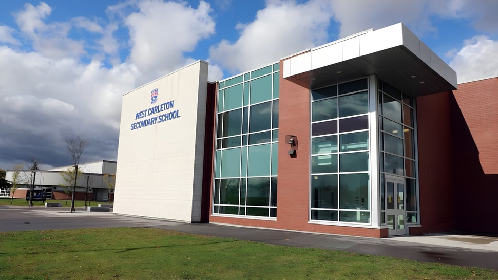 El moderno edificio de varios pisos de la West Carleton Secondary School con grandes ventanales frente a un cielo nublado.