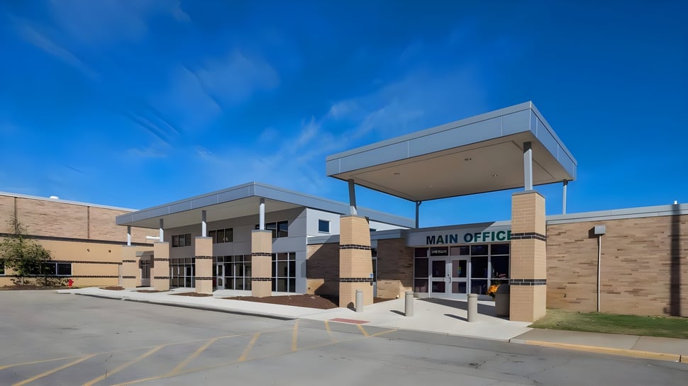 El moderno edificio principal de la West Catholic High School con oficina principal y estacionamiento bajo un cielo despejado.