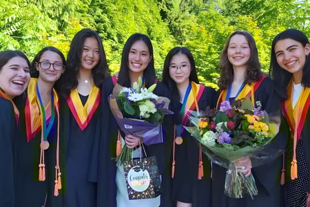 Un grupo de graduadas de la West Vancouver Secondary se encuentra con ramos de flores frente a un fondo verde.