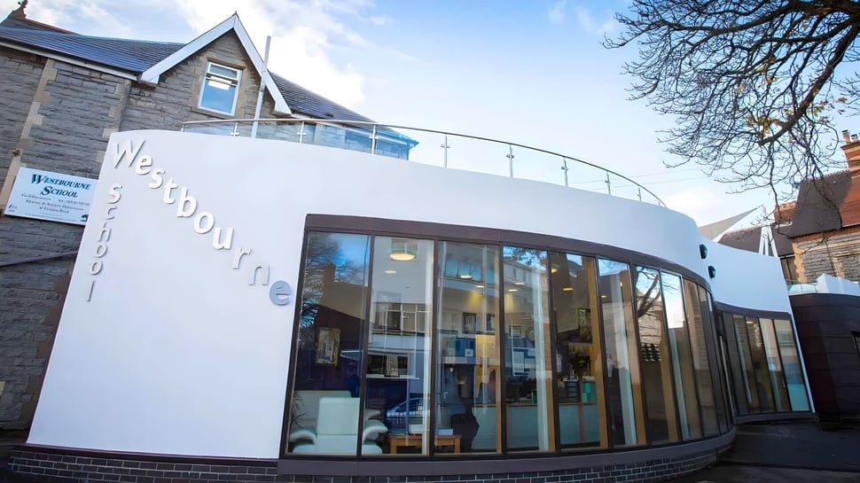 El moderno edificio de la Westbourne School con una fachada de vidrio se encuentra frente a árboles bajo un cielo despejado.
