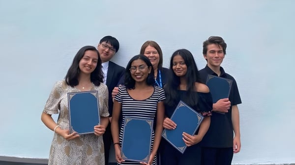 Un grupo de estudiantes de la Westbourne School sostiene carpetas azules frente a un fondo azul claro.