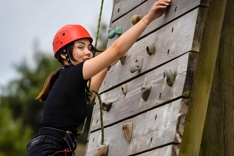 Un estudiante de la Westbourne School escala con un casco rojo en una pared de escalada de madera al aire libre.