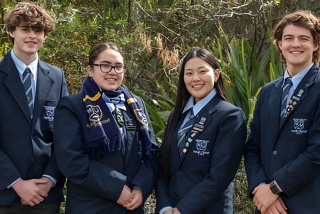Cuatro estudiantes de la Western Heights High School están juntos al aire libre frente a árboles y plantas.