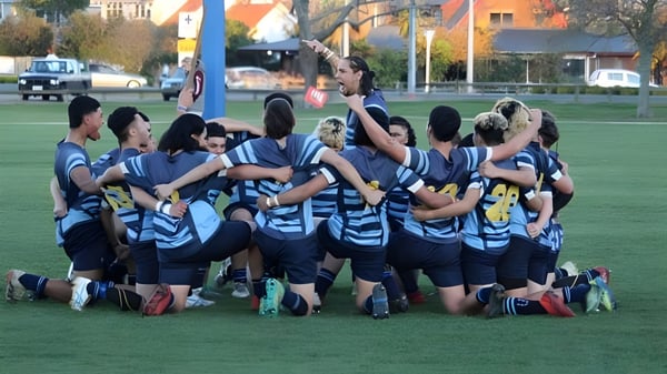 Un grupo de estudiantes en uniformes azules y blancos está en el campo frente al edificio de la Western Heights High School.