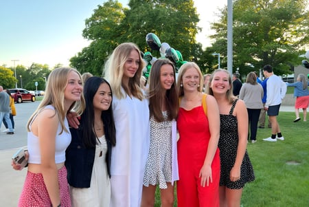 Un grupo de alumnas está en el área exterior de la Western Michigan Christian School frente a árboles y un área de césped.