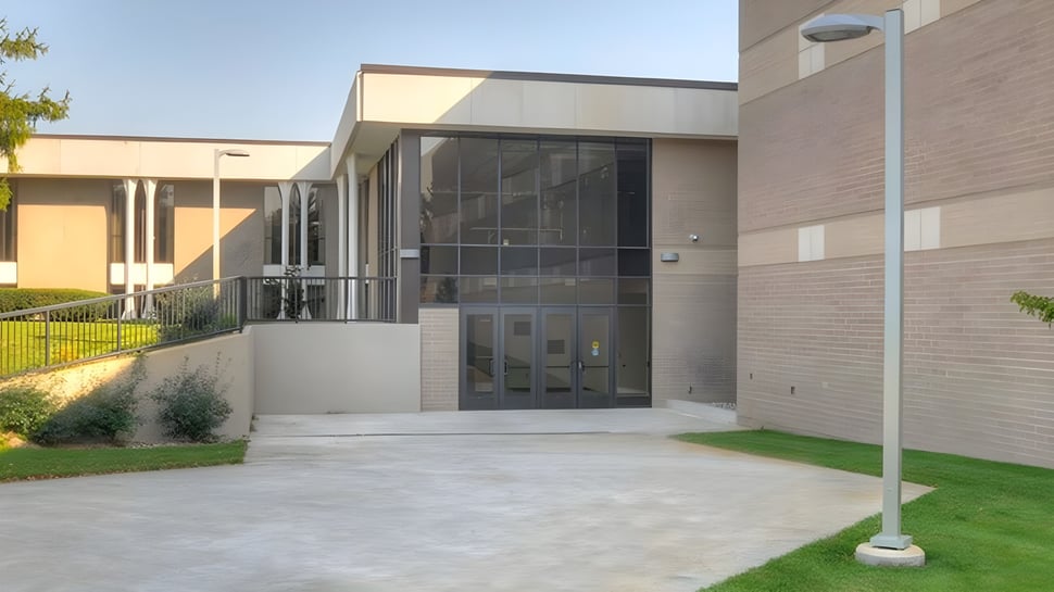 El moderno edificio de la Western Michigan Christian School con fachada de vidrio y una entrada pavimentada bajo un cielo despejado.
