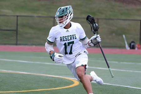 Un deportista con una camiseta blanca de la Western Reserve Academy corre con un stick de lacrosse por el campo.