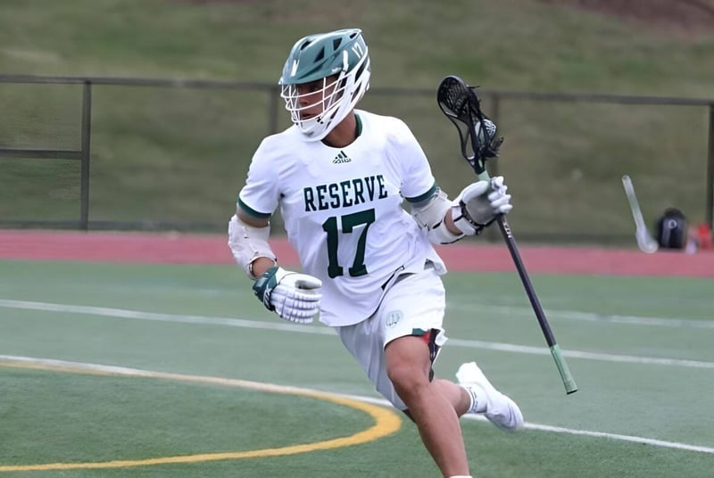 Un deportista con una camiseta blanca de la Western Reserve Academy corre con un stick de lacrosse por el campo.