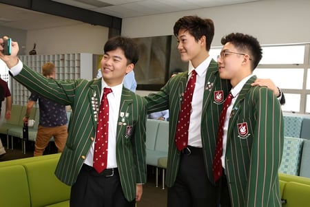 Tres alumnos de la Westlake Boys High School en uniformes escolares posan juntos y sonríen.