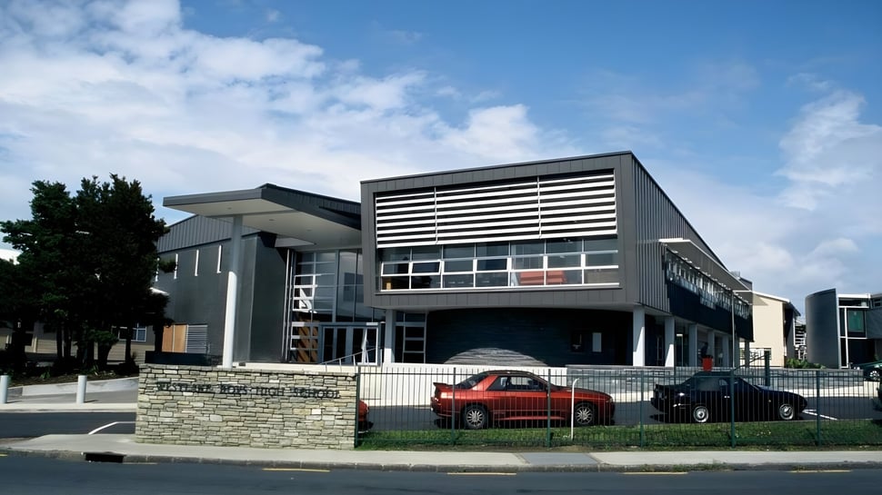 El moderno edificio principal de la Westlake Boys High School con área verde circundante y coches estacionados.