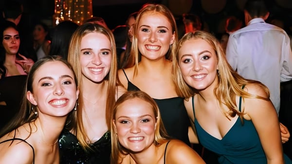 Las estudiantes de la Westlake Girls High School posan juntas en una celebración con iluminación colorida de fondo.