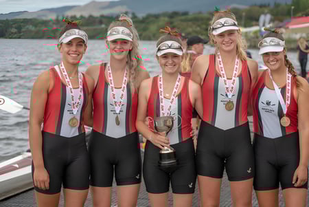 Las estudiantes de la Westlake Girls High School sostienen orgullosamente un trofeo frente a un lago con montañas al fondo.