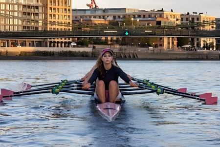 Una persona rema en un bote rosa sobre el agua con el fondo de la Westminster Secondary School al atardecer.
