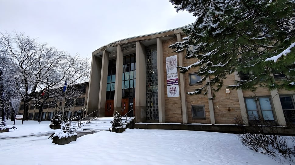 El terreno nevado con la gran construcción de piedra de la Westmount High School en invierno con árboles sin hojas.