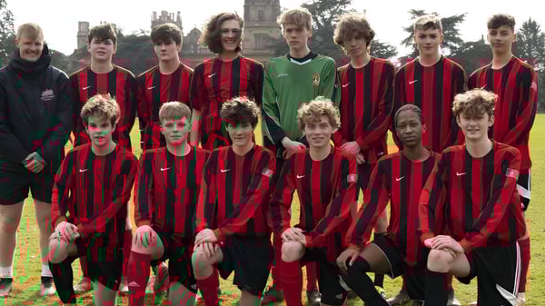 Un grupo de jóvenes futbolistas está en el campo de deportes de Westonbirt School con un campanario de fondo.