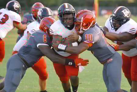 Estudiantes de la Westside Secondary School juegan al fútbol americano en un campo verde bajo un cielo nublado.