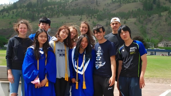 Un grupo de estudiantes de la Westsyde Secondary School posan frente a un panorama montañoso boscoso.