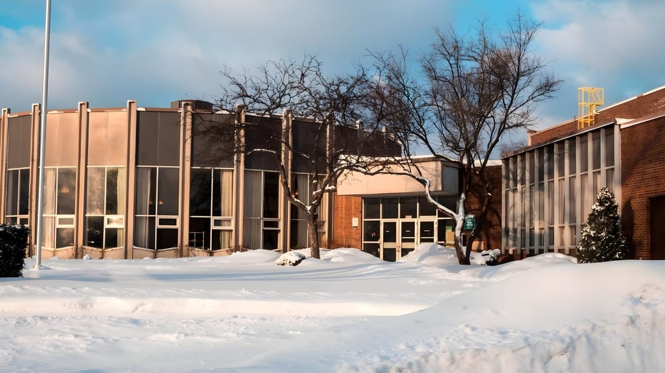 El edificio de ladrillo cubierto de nieve de la Westview Freedom Academy se encuentra frente a árboles desnudos bajo un cielo azul nublado.