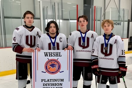 Un grupo de jóvenes jugadores de hockey sostiene un banner de la WESHL Platinum Division frente a una sala de hielo en el Westwood Collegiate.