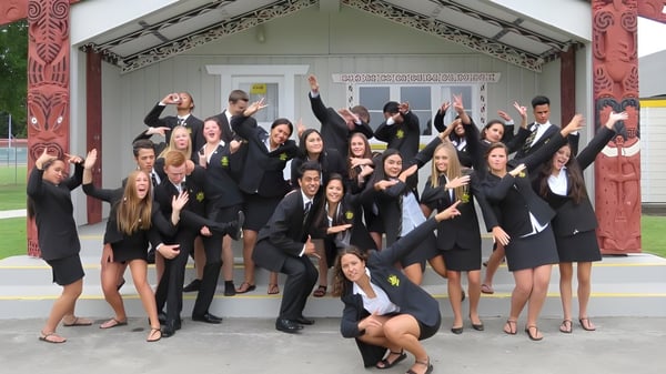 Un grupo de graduados de la Whakatane High School celebra frente a una casa de reunión maorí tradicional con tallas.