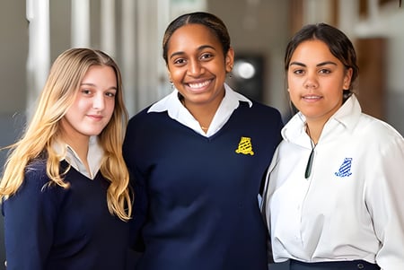 Tres estudiantes están juntos en el pasillo del Whanganui Girls’ College y llevan uniformes escolares.