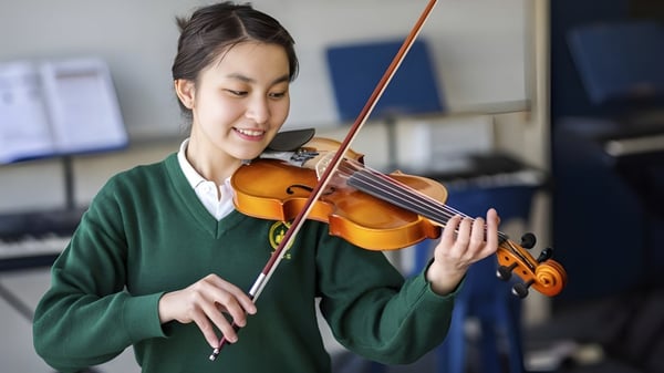 Una estudiante de la Whanganui High School toca el violín frente a instrumentos musicales en el fondo.