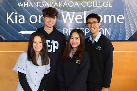 Un grupo de cuatro estudiantes posa frente a un banner que dice 'Kia ora Welcome' en el campus de Whangaparāoa College.